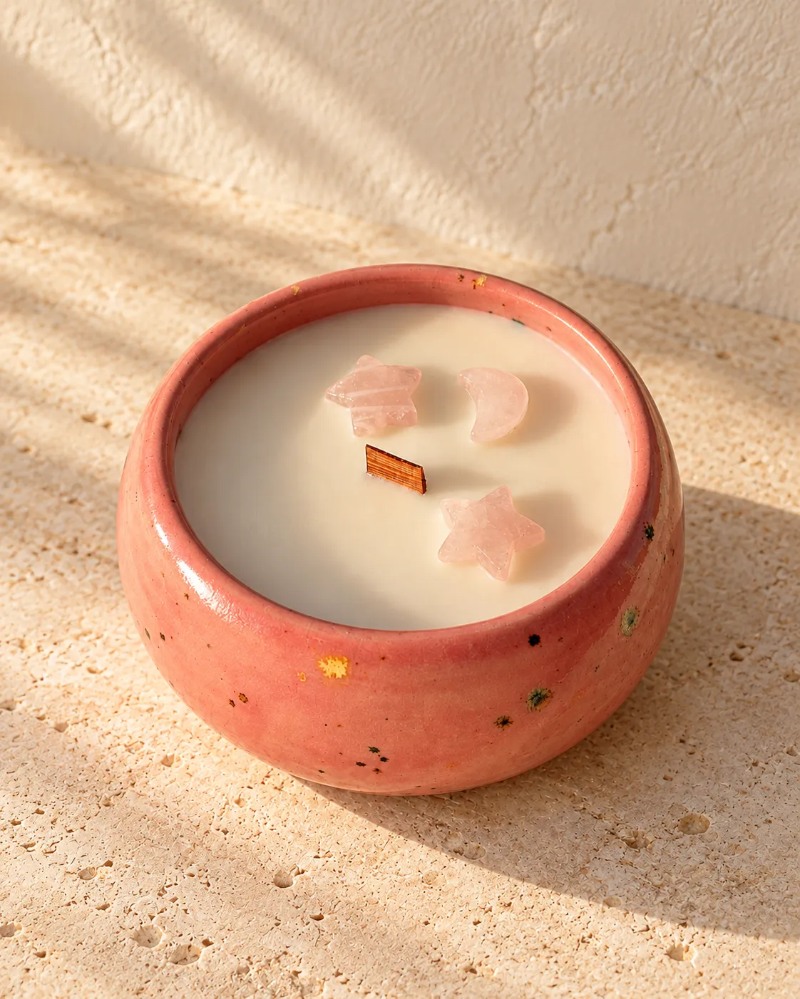 A rose-pink speckled ceramic candle with a wooden wick and two rose-quartz stars and a moon set into the wax