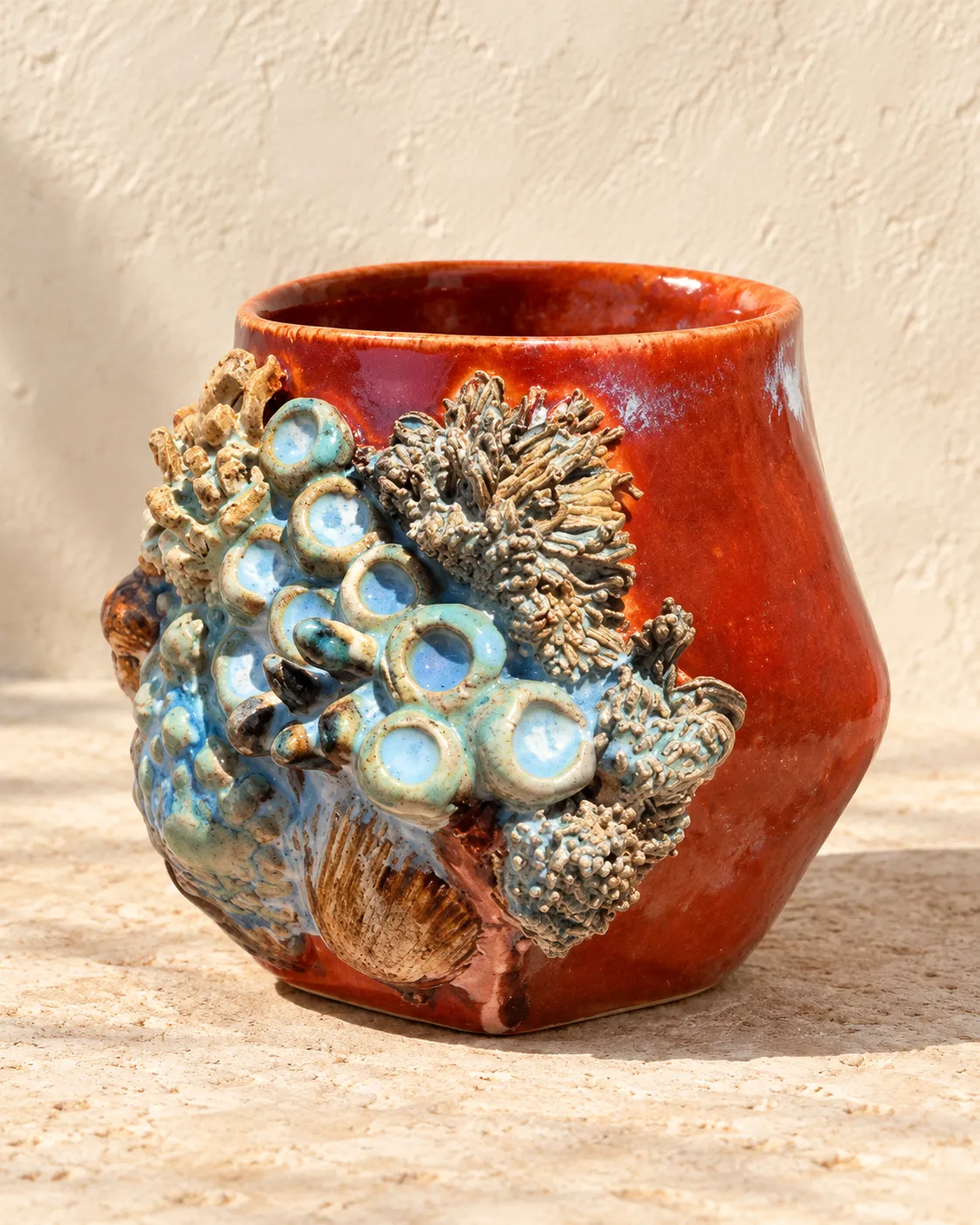 A red-glazed vessel with a sculpted cluster of coral, barnacles and a shell down one side