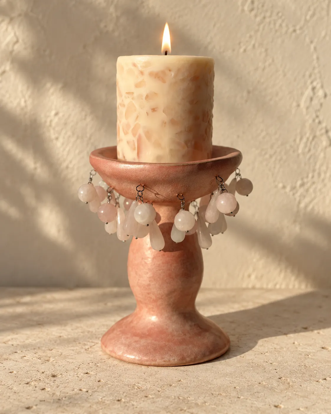 A rose-pink footed candle holder hung with rose-quartz drops, a candle burning in it