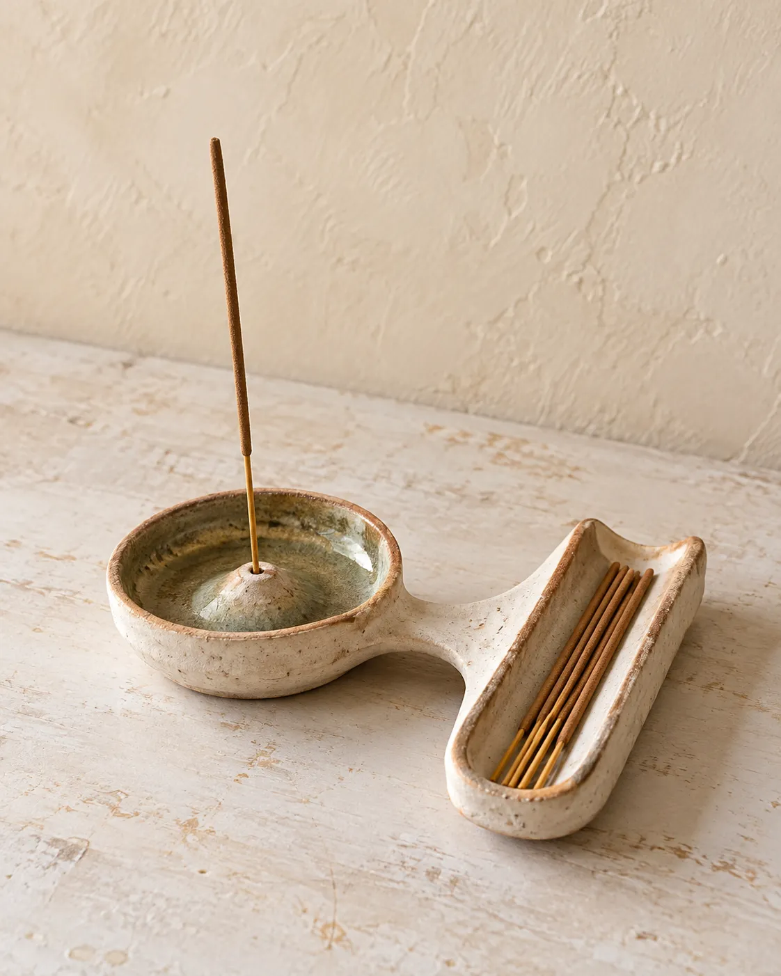 An incense holder with a stick burning in it, beside a long stick tray