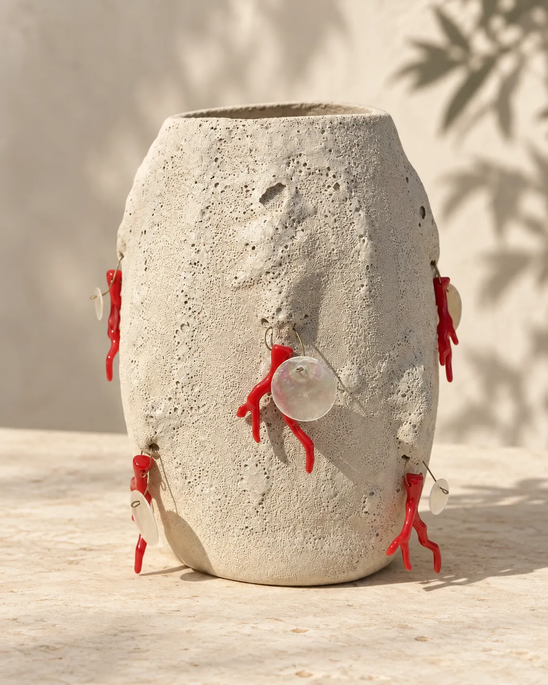 A textured stone-like vase hung with red coral and mother-of-pearl charms